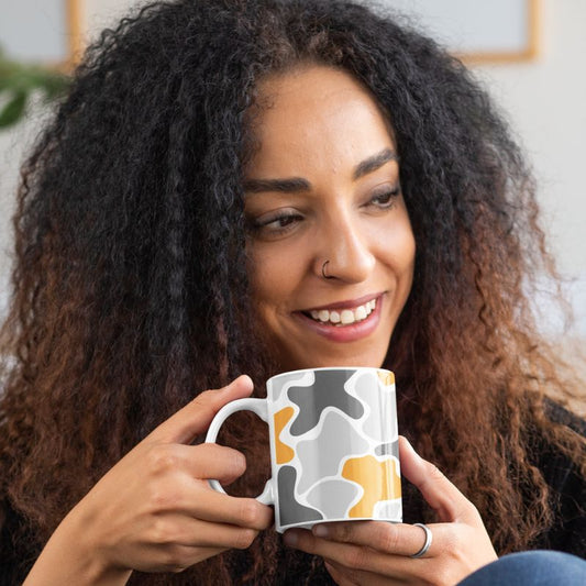 Smiling woman holding a white ceramic mug with an abstract gray and mustard-yellow pattern.