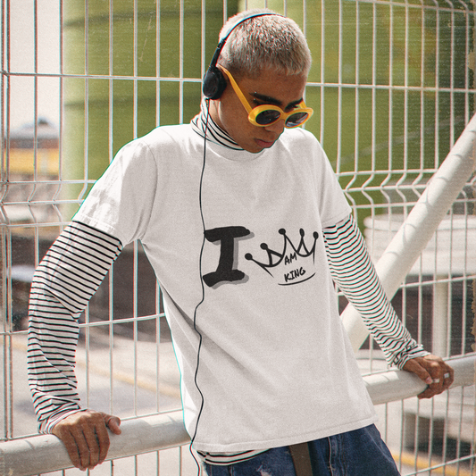 Person wearing a white long-sleeve shirt with text, blue jeans, and sunglasses, leaning against a metal railing with a green industrial building in the background.