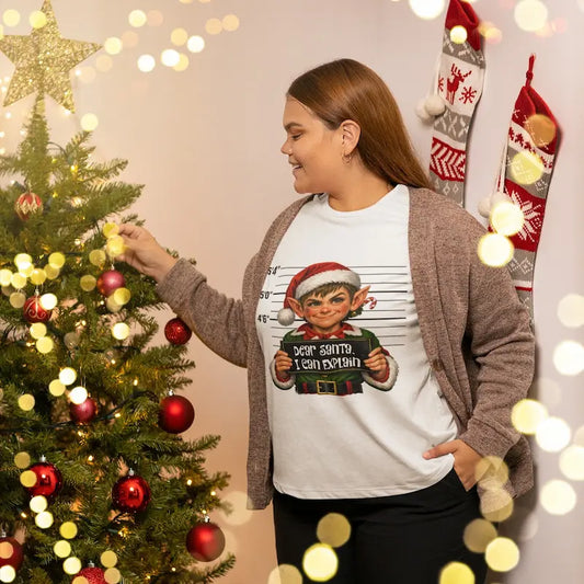 Woman in a white Dear Santa I Can Explain elf t-shirt decorating a Christmas tree