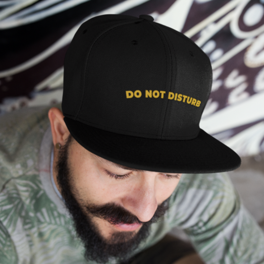 Do Not Disturb embroidered snapback cap in black — gold lettering on male model against urban graffiti wall