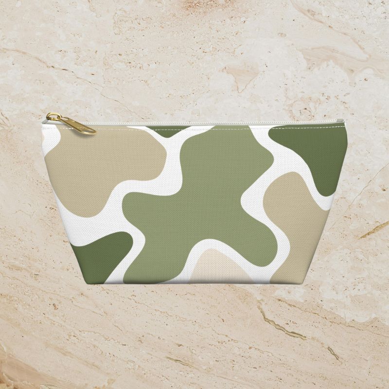 Sage green, tan, and white abstract camouflage pouch on a warm beige stone background.