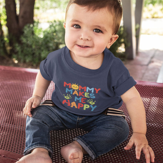 Smiling baby boy wearing navy Mommy Makes Me Happy graphic tee seated outdoors on a picnic table
