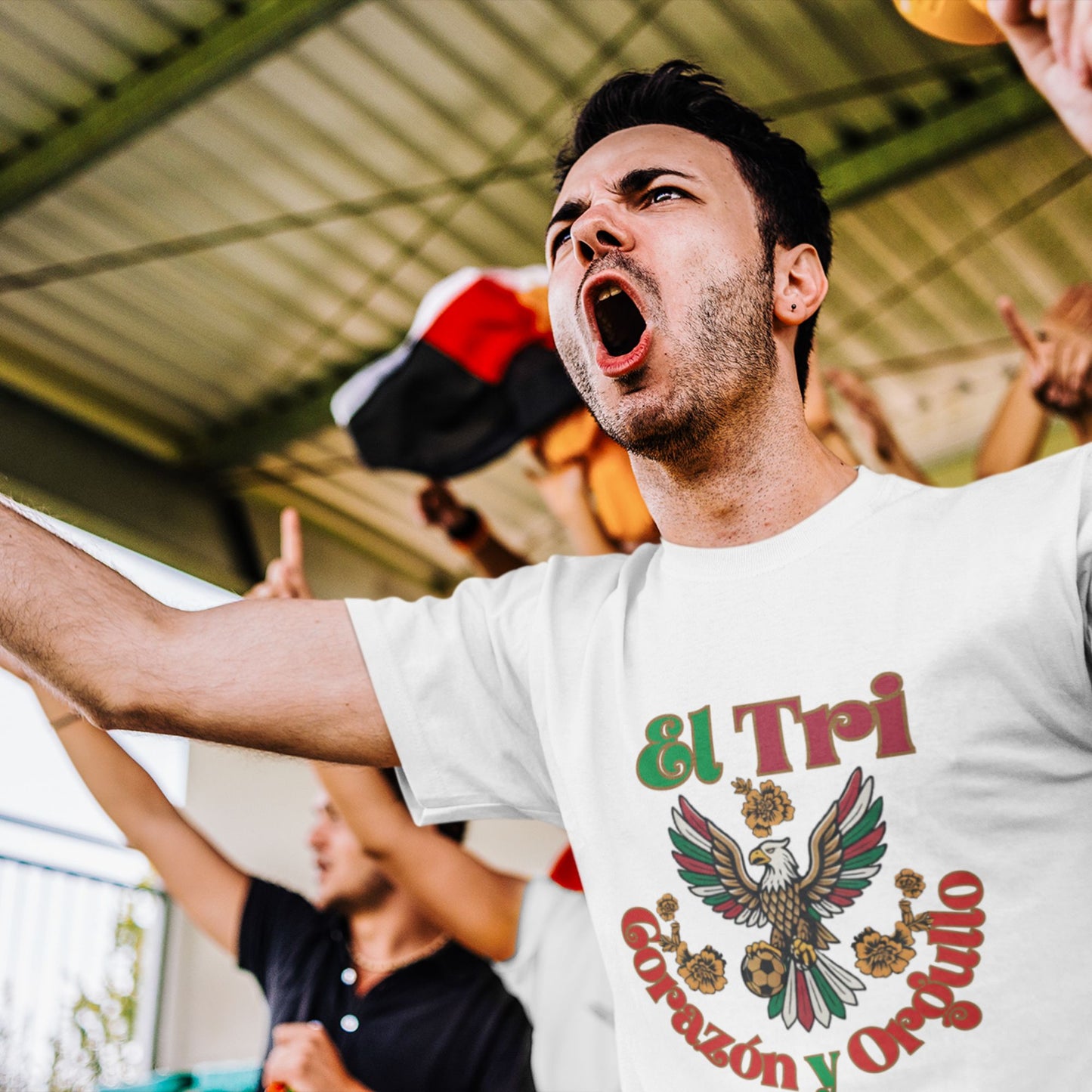 Man cheering at stadium in white El Tri Corazón y Orgullo graphic tee, fan energy lifestyle shot
