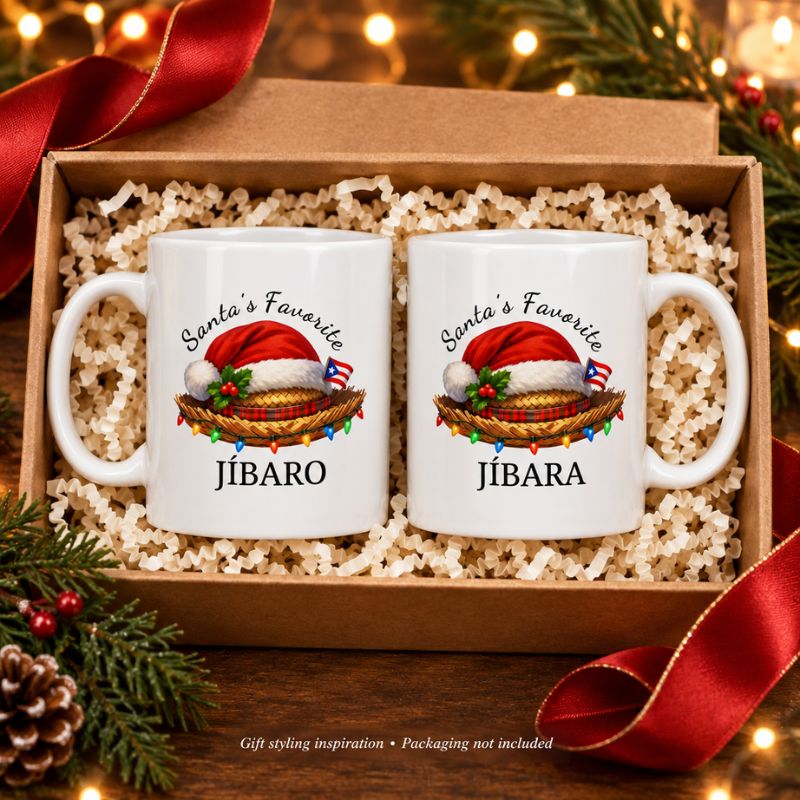 Santa’s Favorite Jíbaro and Jíbara white mugs displayed together in an open kraft box with shredded paper, red ribbon, and Christmas greenery. Gift packaging not included.