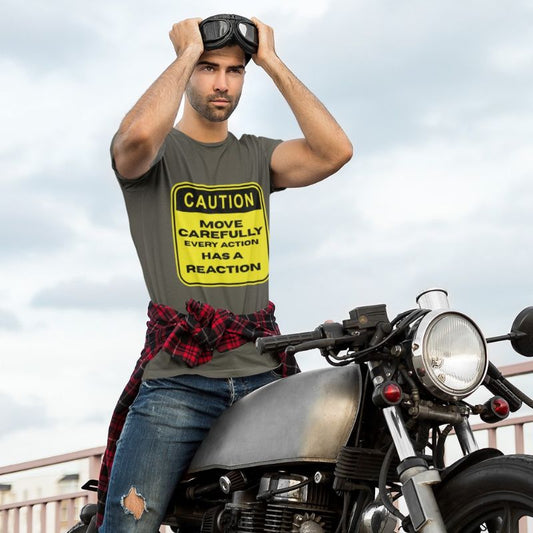 Man sitting on a motorcycle wearing an Army olive t-shirt with a yellow Caution Move Carefully Every Action Has a Reaction graphic.