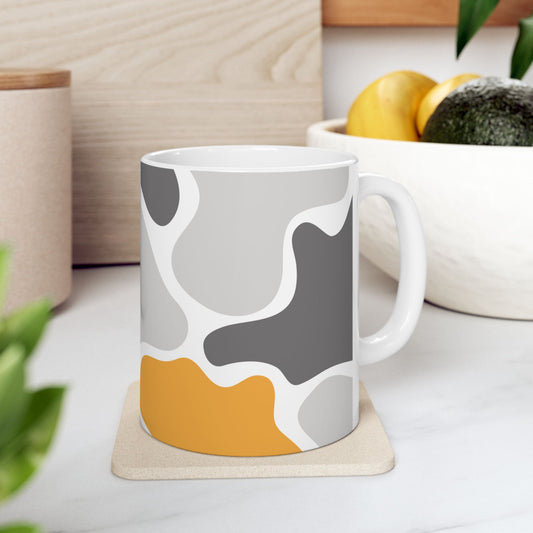 White ceramic mug with an abstract gray, white, and mustard-yellow pattern, resting on a coaster on a kitchen counter.
