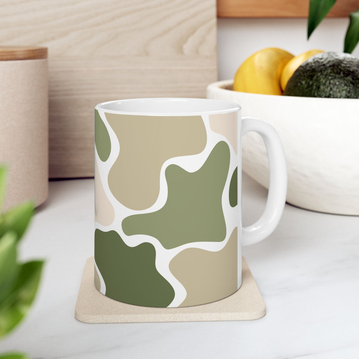  Green and beige camouflage mug with a white handle on a coaster on a kitchen counter.