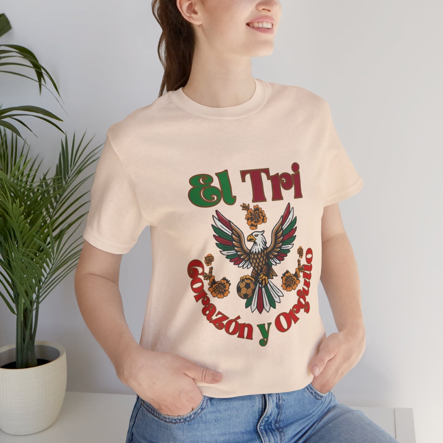 Woman wearing soft cream El Tri Corazón y Orgullo tee outdoors, casual lifestyle shot
