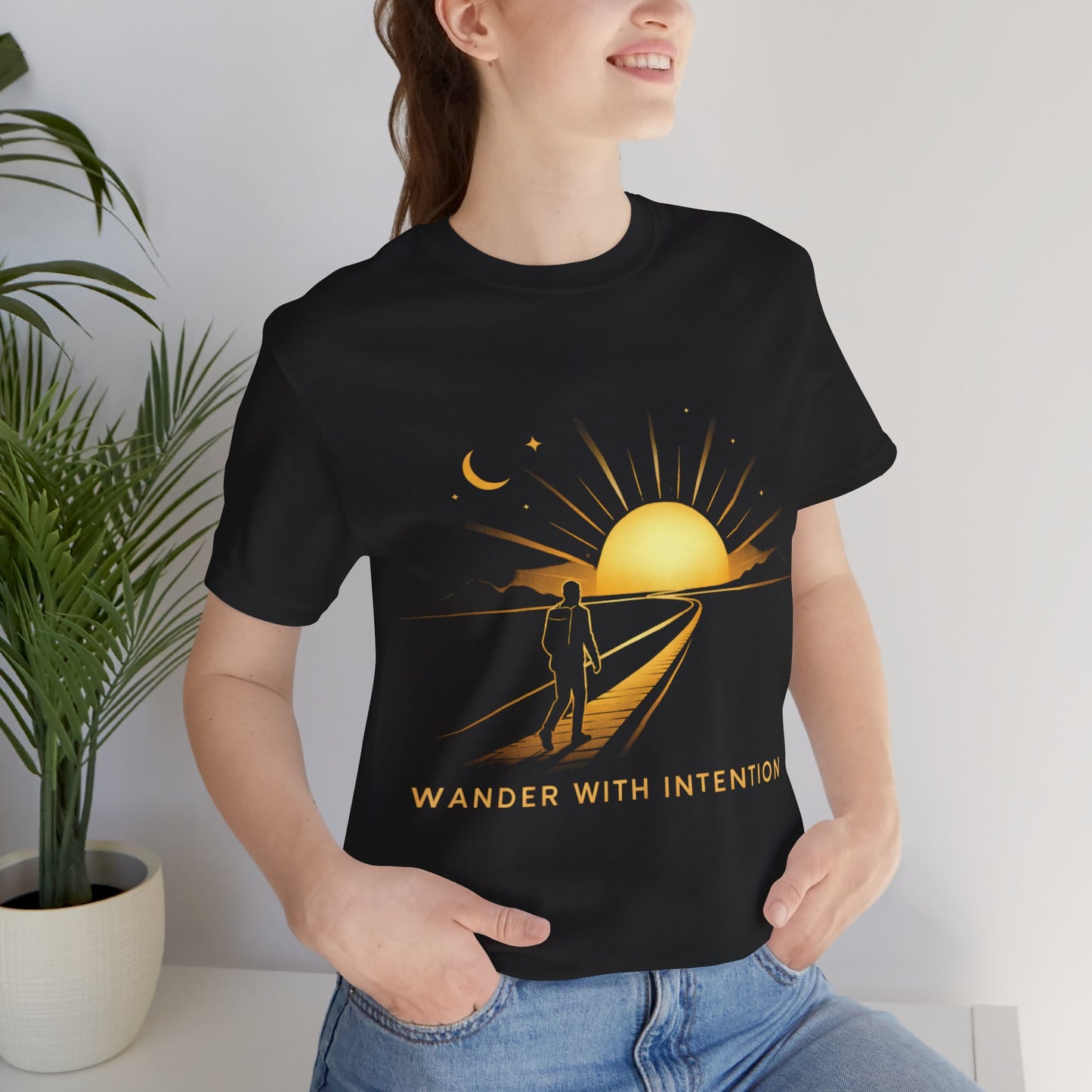 Woman wearing black Wander With Intention sunset graphic tee, indoor casual lifestyle shot

