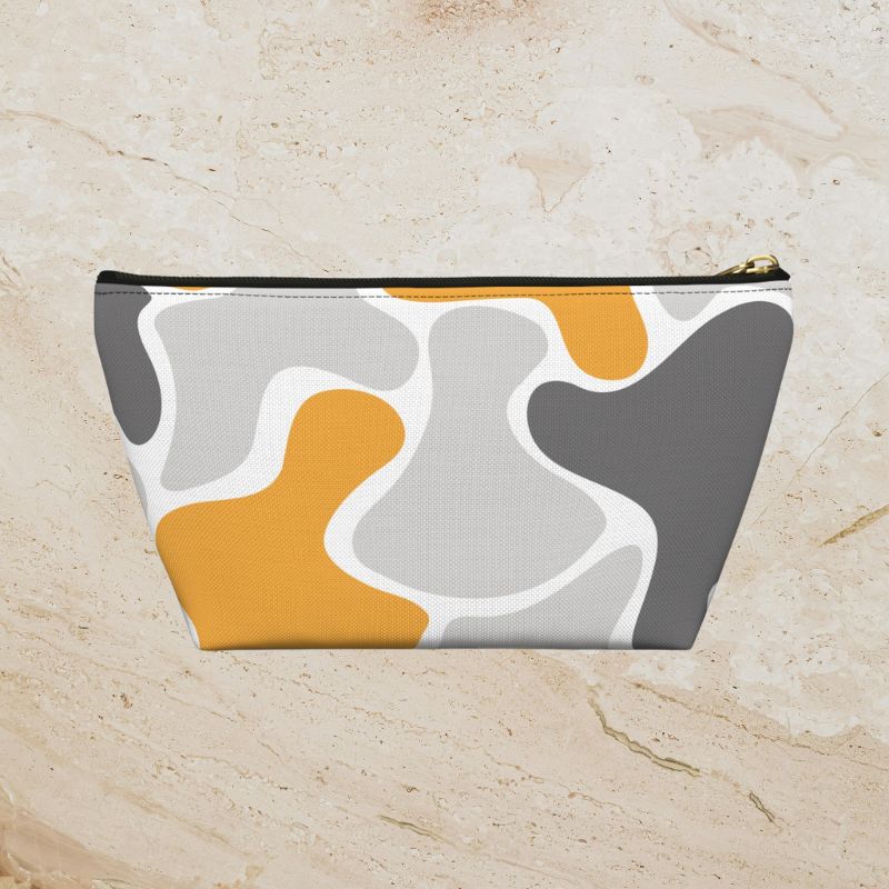 Yellow, gray, and white abstract camouflage zipper pouch on a warm beige stone background.