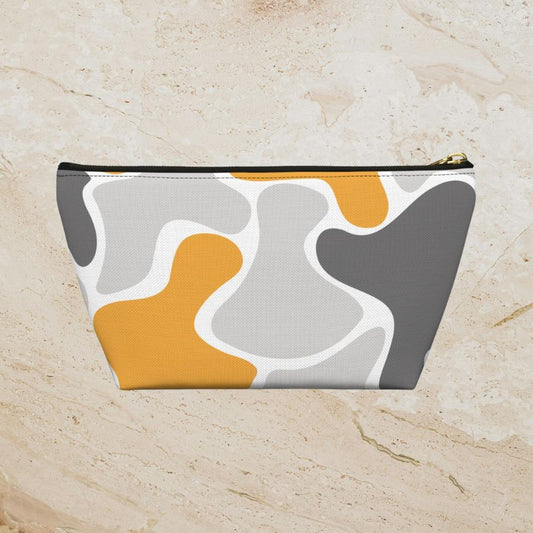 Yellow, gray, and white abstract camouflage zipper pouch on a warm beige stone background.