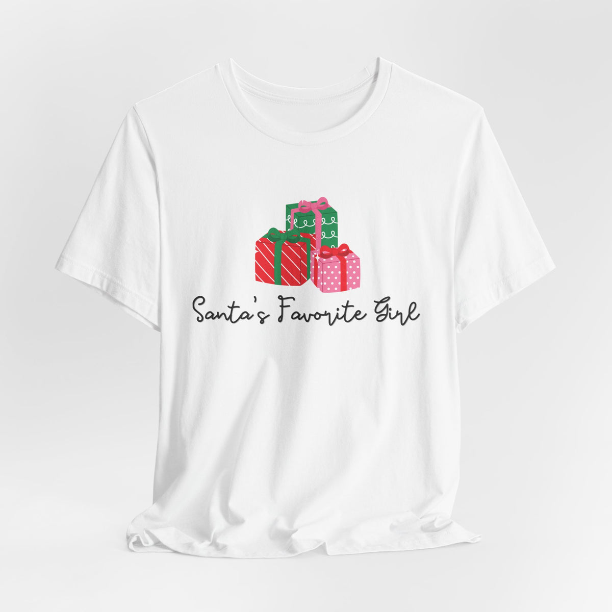 A white short-sleeve crewneck t-shirt featuring a graphic of three Christmas presents in red, green, and pink with the text 'Santa's Favorite Girl' printed below in black cursive, displayed on a light gray background.