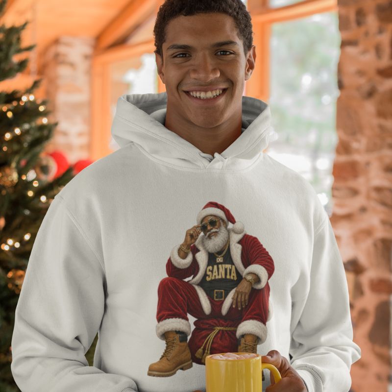 Man wearing a white OG Santa Christmas hoodie and holding a yellow mug beside a decorated Christmas tree.
