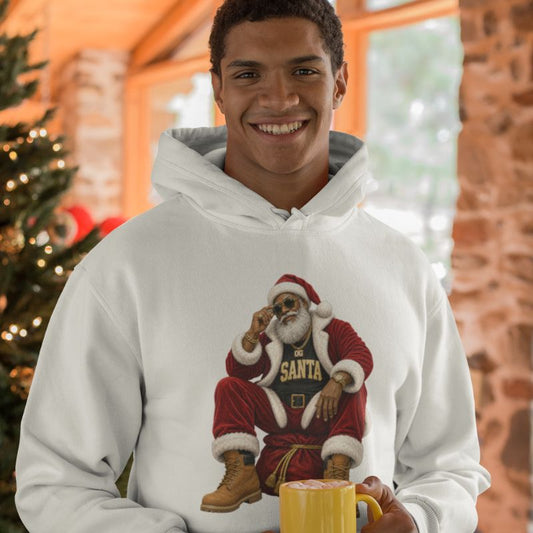 Man wearing a white OG Santa Christmas hoodie and holding a yellow mug beside a decorated Christmas tree.