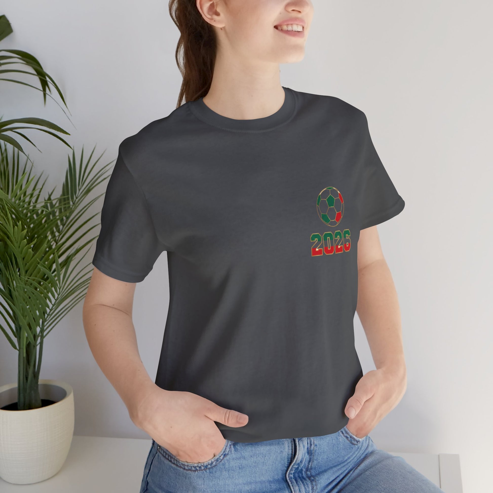Woman wearing charcoal El Tri soccer tee with left chest logo, casual indoor lifestyle shot
