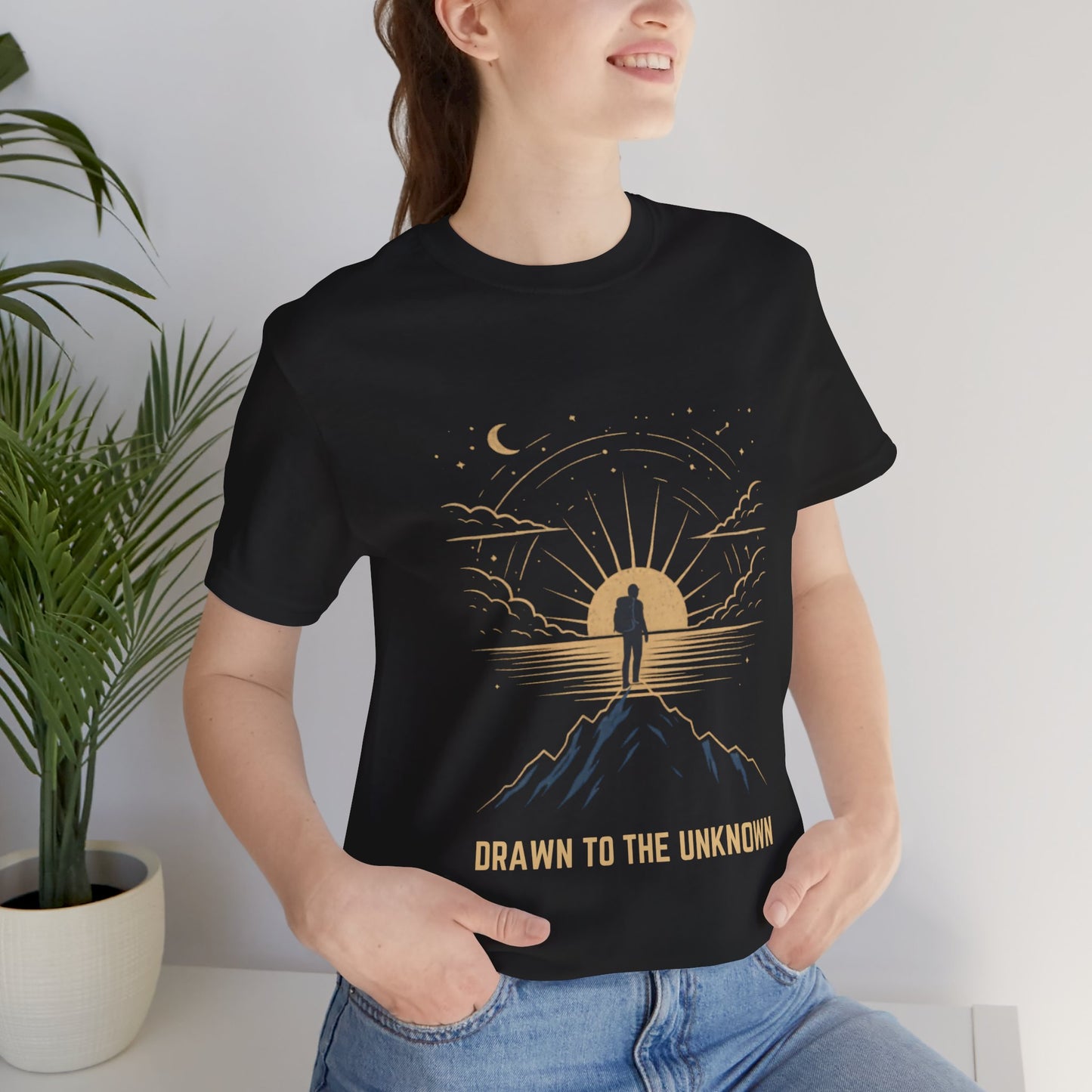 Woman wearing Drawn to the Unknown black graphic tee indoors with plants — unisex celestial adventure graphic tee


