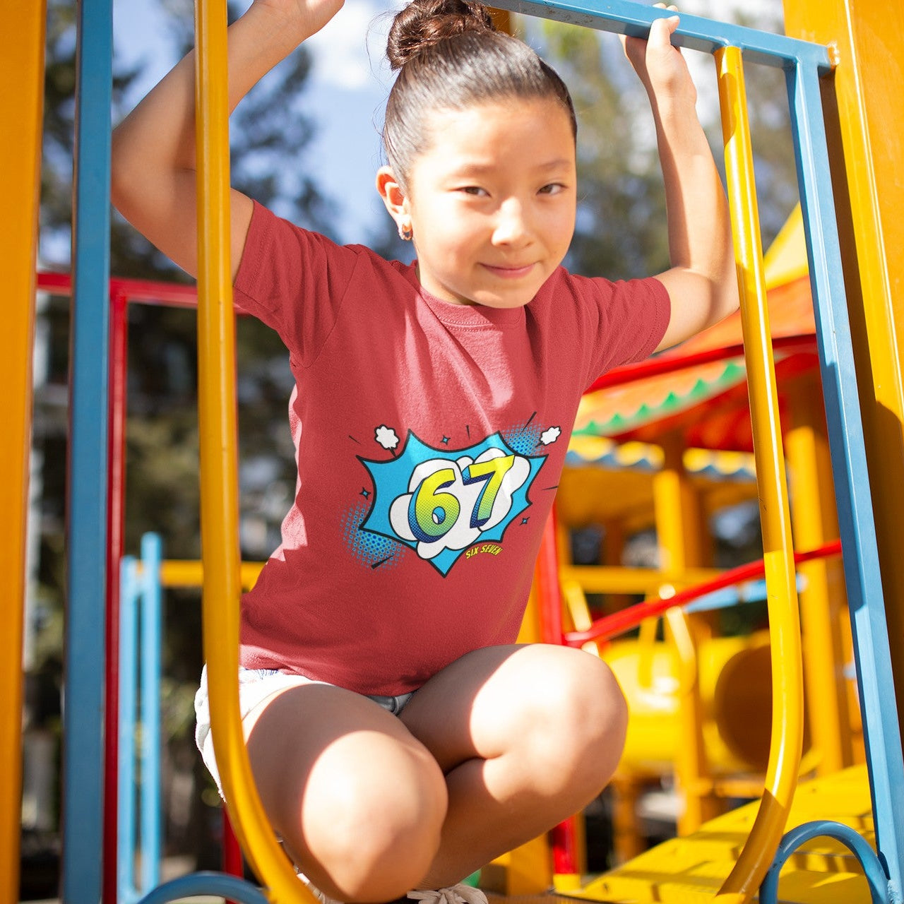 Girl wearing Kids Six Seven Comic Pop Graphic T-Shirt in Red, playing on playground