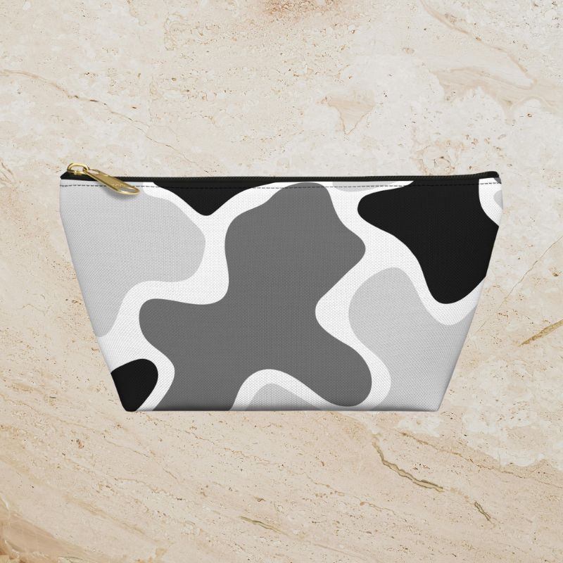Black, gray, and white abstract camouflage pouch on a warm beige stone background.