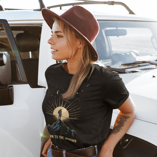 Woman in cowboy hat wearing Drawn to the Unknown black graphic tee outdoors — celestial mountain adventure shirt

