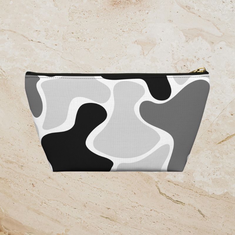 Black, gray, and white abstract camouflage pouch on a warm beige stone background.