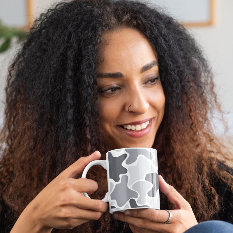 Smiling woman holding a white mug with a black and gray abstract pattern.