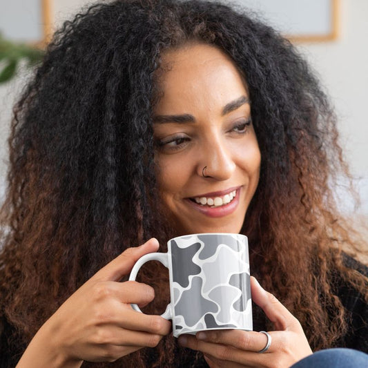 Smiling woman holding a white mug with a black and gray abstract pattern.
