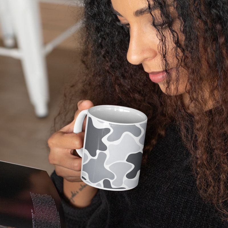 Woman looking down at a white mug with a black and gray abstract pattern.