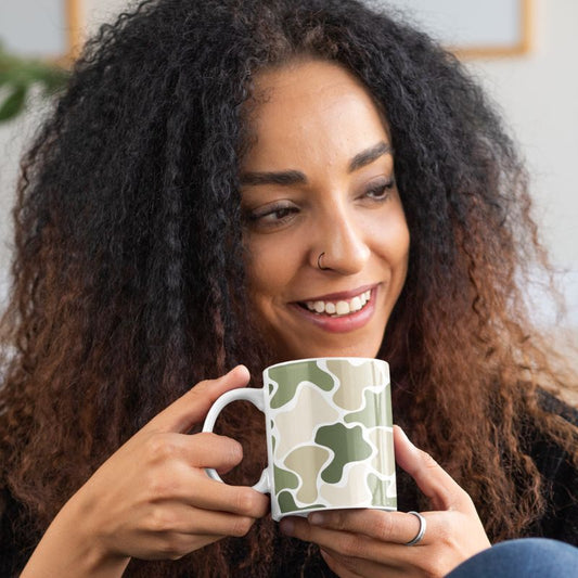 Woman smiling while holding a green and beige camouflage mug with a white handle.