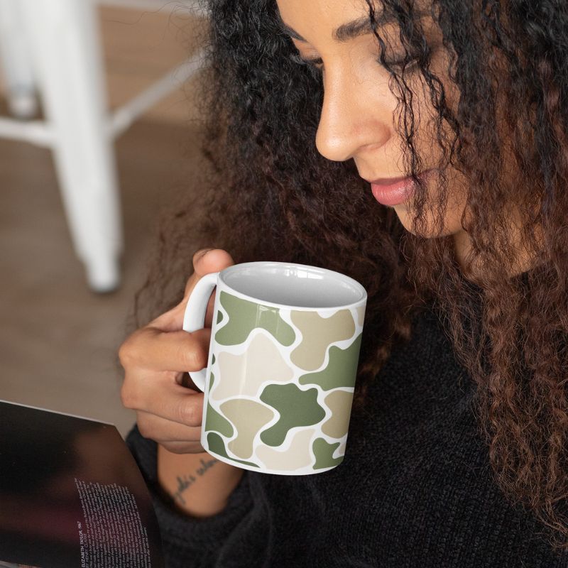Woman lifting a green and beige camouflage mug toward her lips.