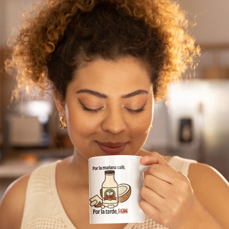 Woman holding a white “Por la mañana café. Por la tarde, RON” mug near her face.