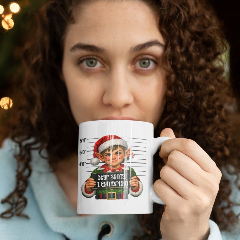Woman sipping from a white Christmas mug featuring an elf holding a “Dear Santa, I can explain” sign.