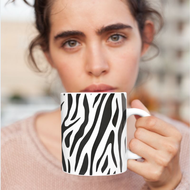 Close-up of a person holding a black-and-white zebra print mug near their face.