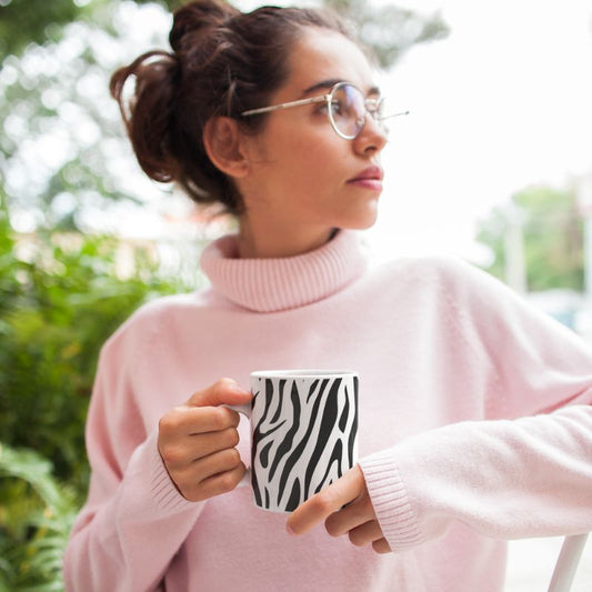 Person in a pink sweatshirt holding a black-and-white zebra print mug outdoors.