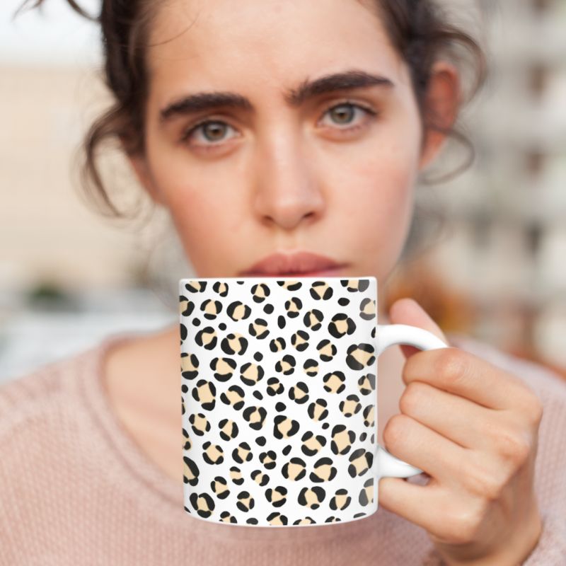 Close-up of a woman holding a white mug with a black leopard-print pattern near her face.