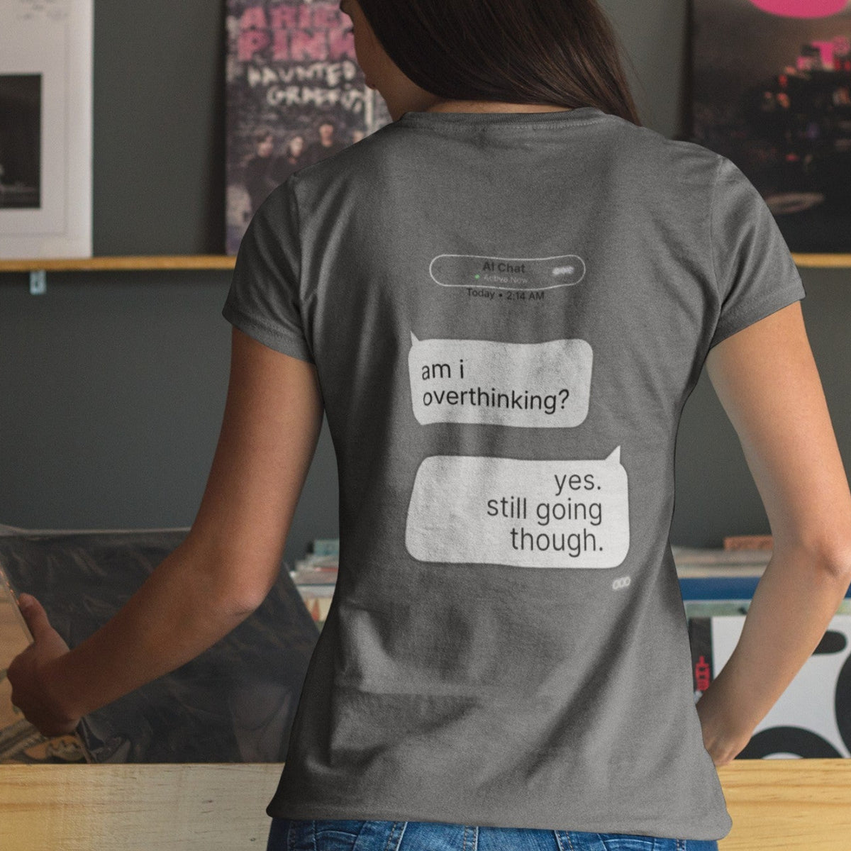 Woman showing back print of Am I Overthinking AI chat graphic tee in asphalt gray in record store setting
