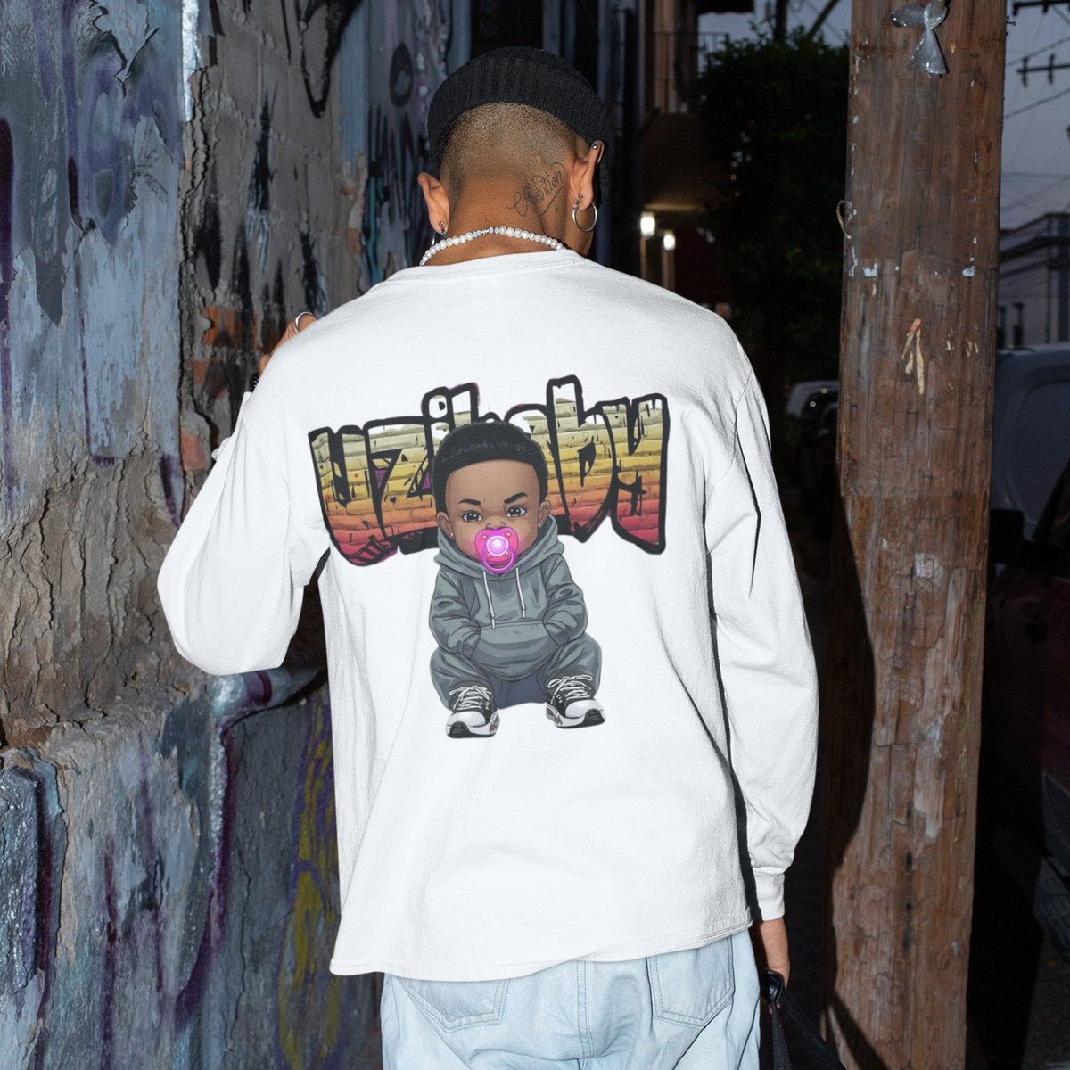 Back view of a person walking down a dark street in a white Uzi Baby long-sleeve t-shirt with the Uzi Baby