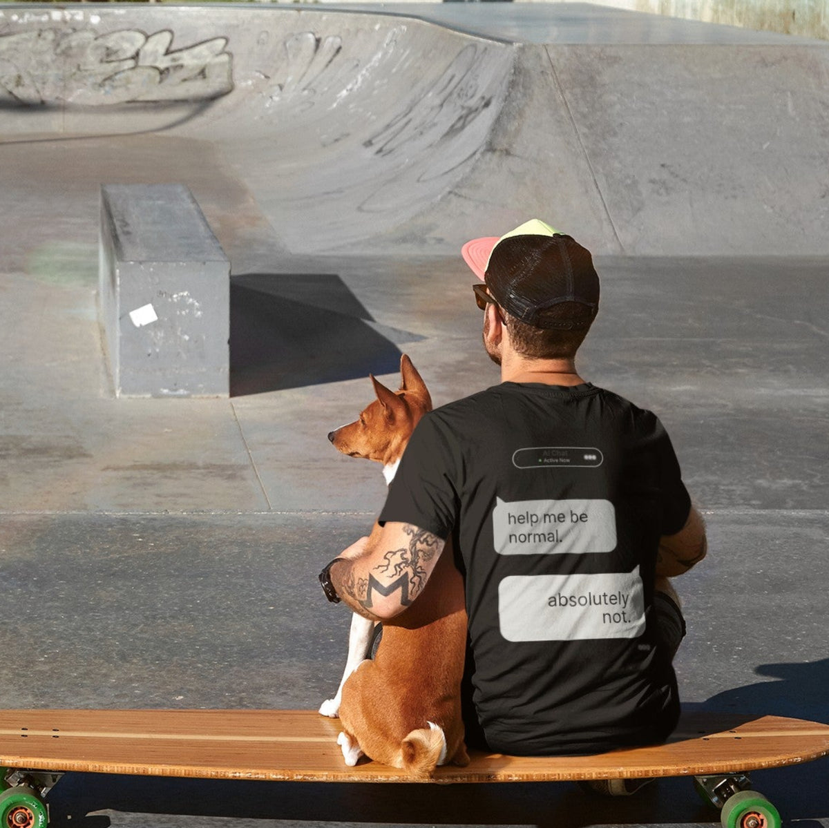 Man and dog sitting on longboard at skate park showing back print of Help Me Be Normal AI chat graphic tee in black
