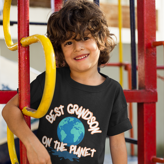 Child wearing a black t-shirt with 'Best Grandson on the Planet' text at a playground.