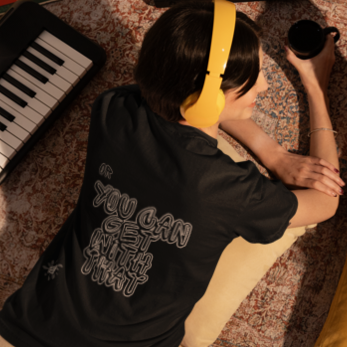 You Can Get With This back print graphic tee — overhead view on female model with yellow headphones in music room setting