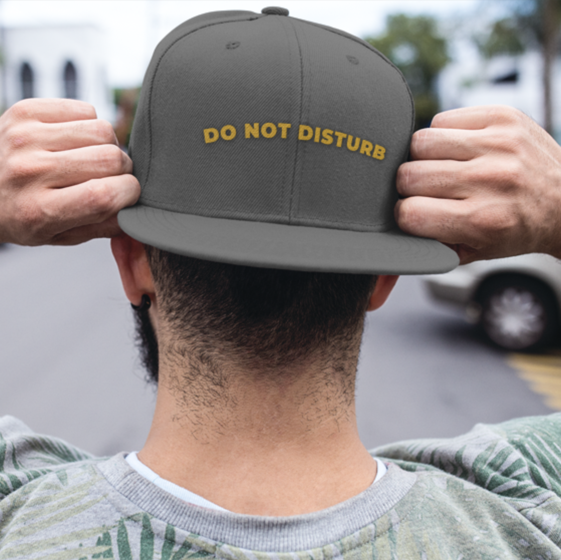 Do Not Disturb snapback cap in gray — gold embroidered lettering worn by male model on urban street