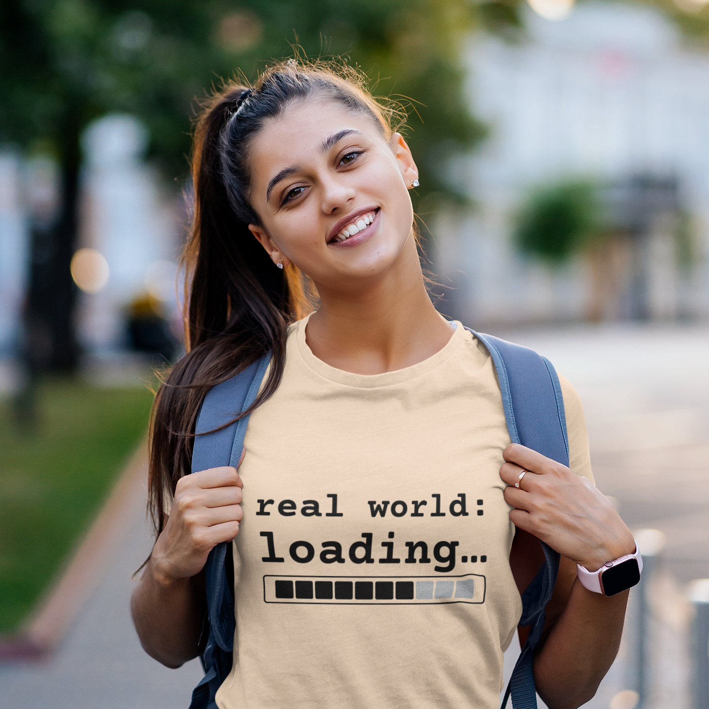 Woman wearing Soft Cream real world loading graphic tee outdoors with backpack — streetwear graduation lifestyle shot