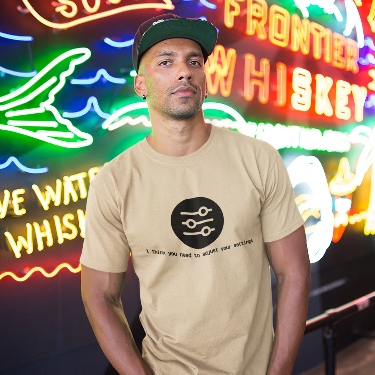 Man in a snapback wearing a soft cream Adjust Your Settings t-shirt with a settings slider graphic against neon lights