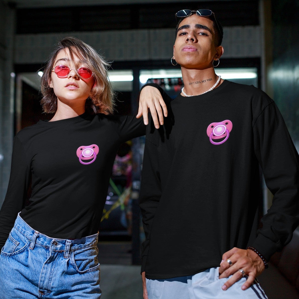 Man and woman wearing black Uzi Baby long-sleeve t-shirts with a pink pacifier graphic on the chest