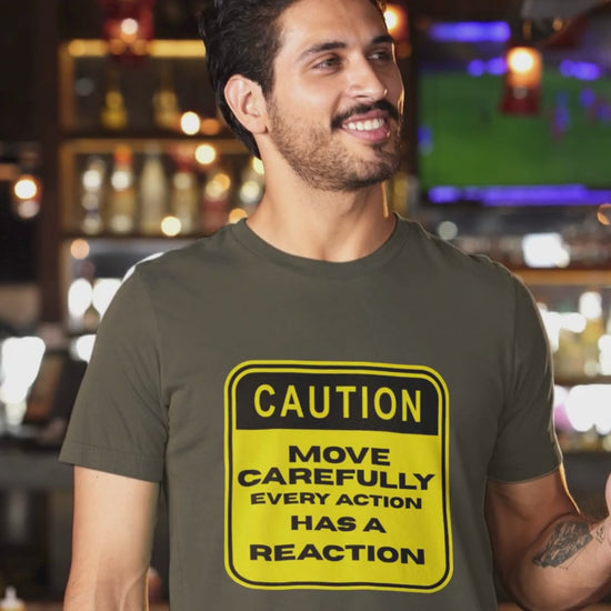 Smiling man in a bar wearing an Army olive t-shirt with a yellow Caution Move Carefully Every Action Has a Reaction graphic