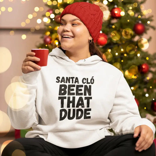 Woman wearing a white Santa Cló Been That Dude Christmas hoodie beside a decorated Christmas tree