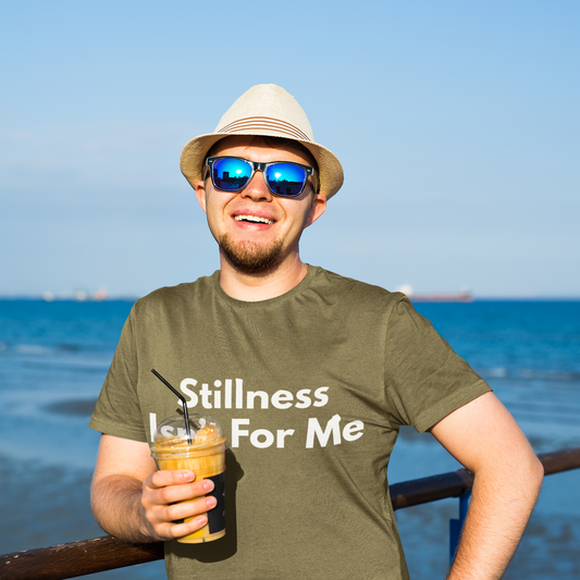 Man at waterfront wearing cream Stillness Isn't For Me graphic tee — restless soul adventure shirt
