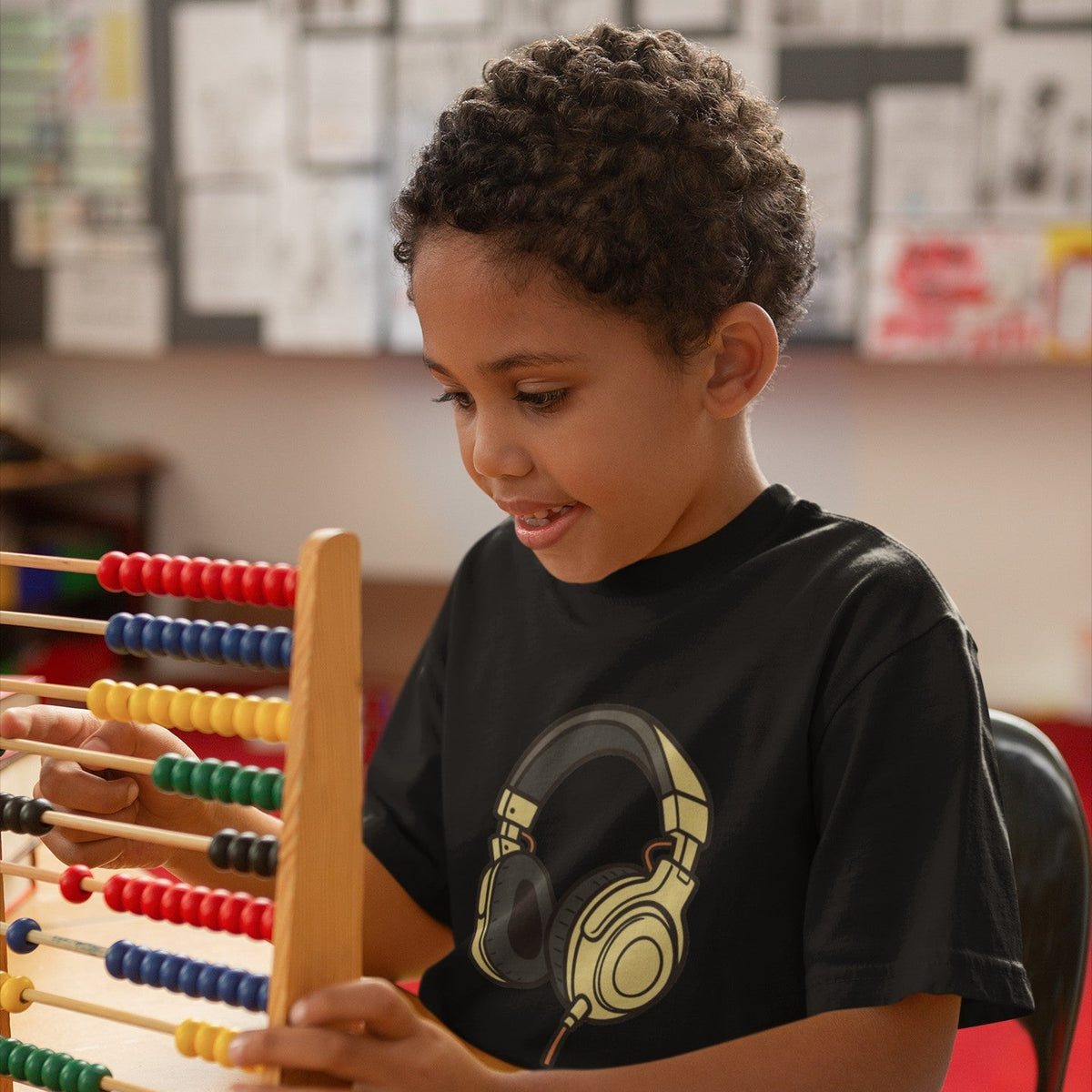 Young boy focused on an abacus in a classroom wearing a black kids gold DJ headphones graphic t-shirt — Leela's Ink

