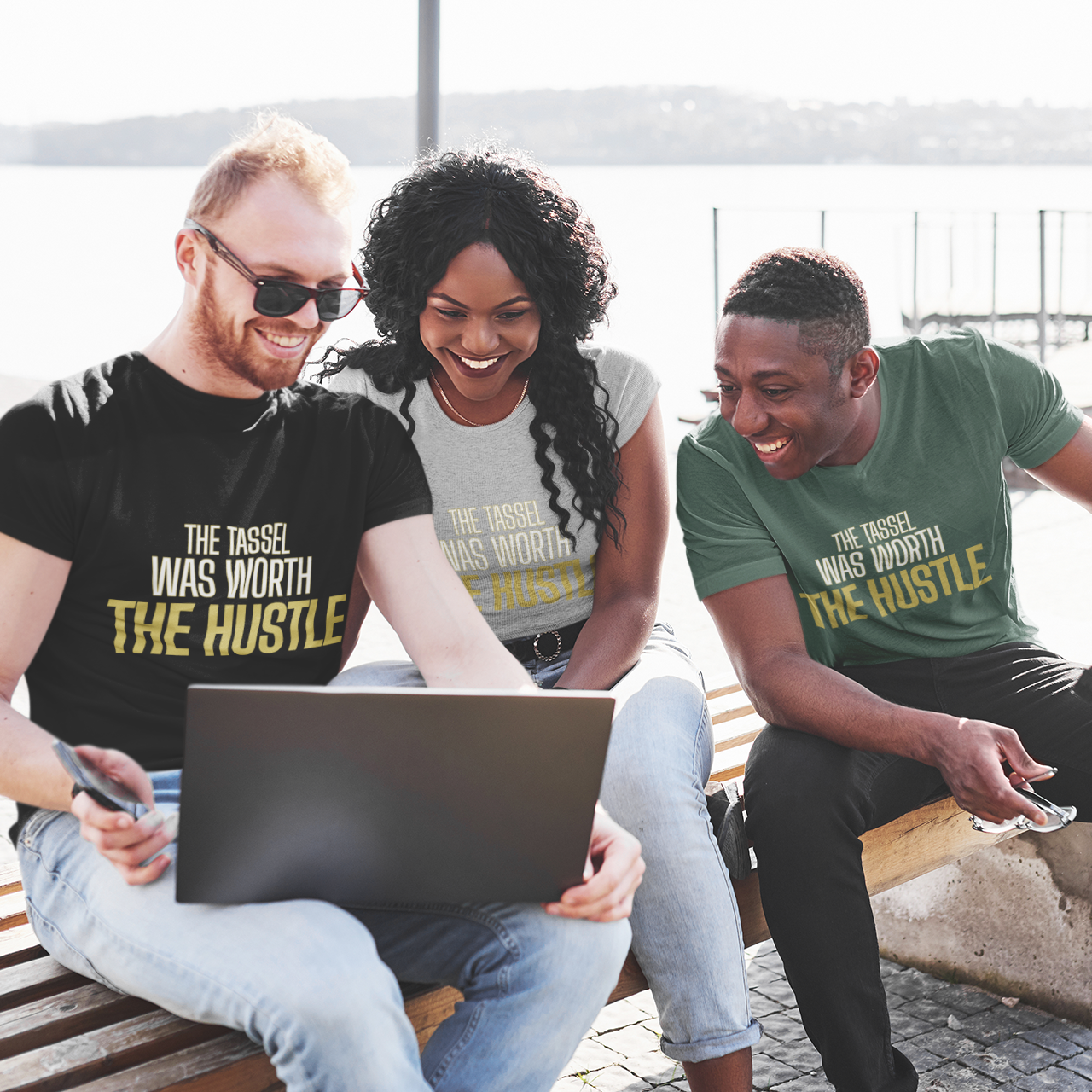 Three friends wearing The Tassel Was Worth The Hustle graduation tees at waterfront — grad celebration streetwear
