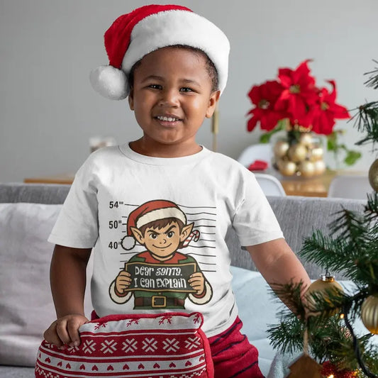 Smiling boy in a Santa hat wearing a white Dear Santa I Can Explain kids Christmas elf t-shirt