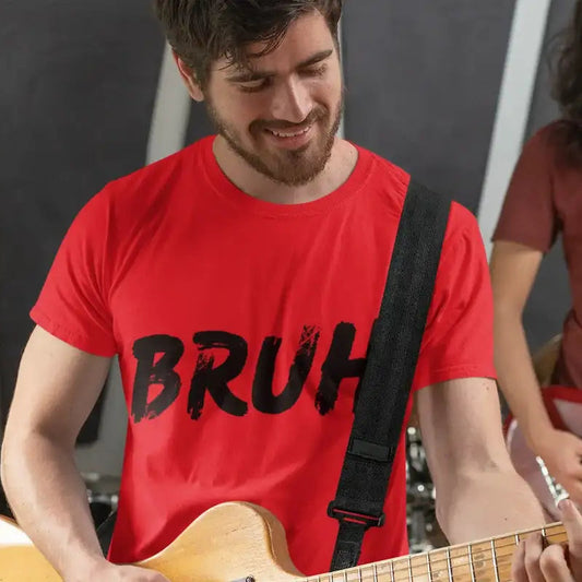 A man in a red t-shirt with 'BRUH' printed in black distressed lettering, playing a light-colored bass guitar in a music studio setting with another musician blurred in the background.